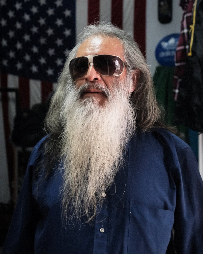 Hombre con una larga barba blanca con una bandera de Estados Unidos de fondo