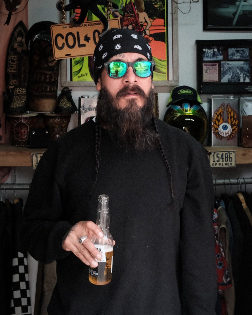 Hombre de barba larga y oscura con una cerveza en la mano y lentes de sol