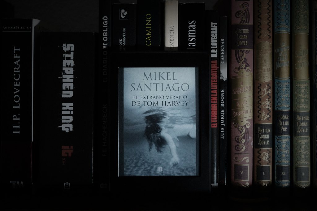Estantería de libros con una novela de Mikel Santiago al centro, fotografiada con luz tenue como símbolo de volver al hábito de la lectura.
